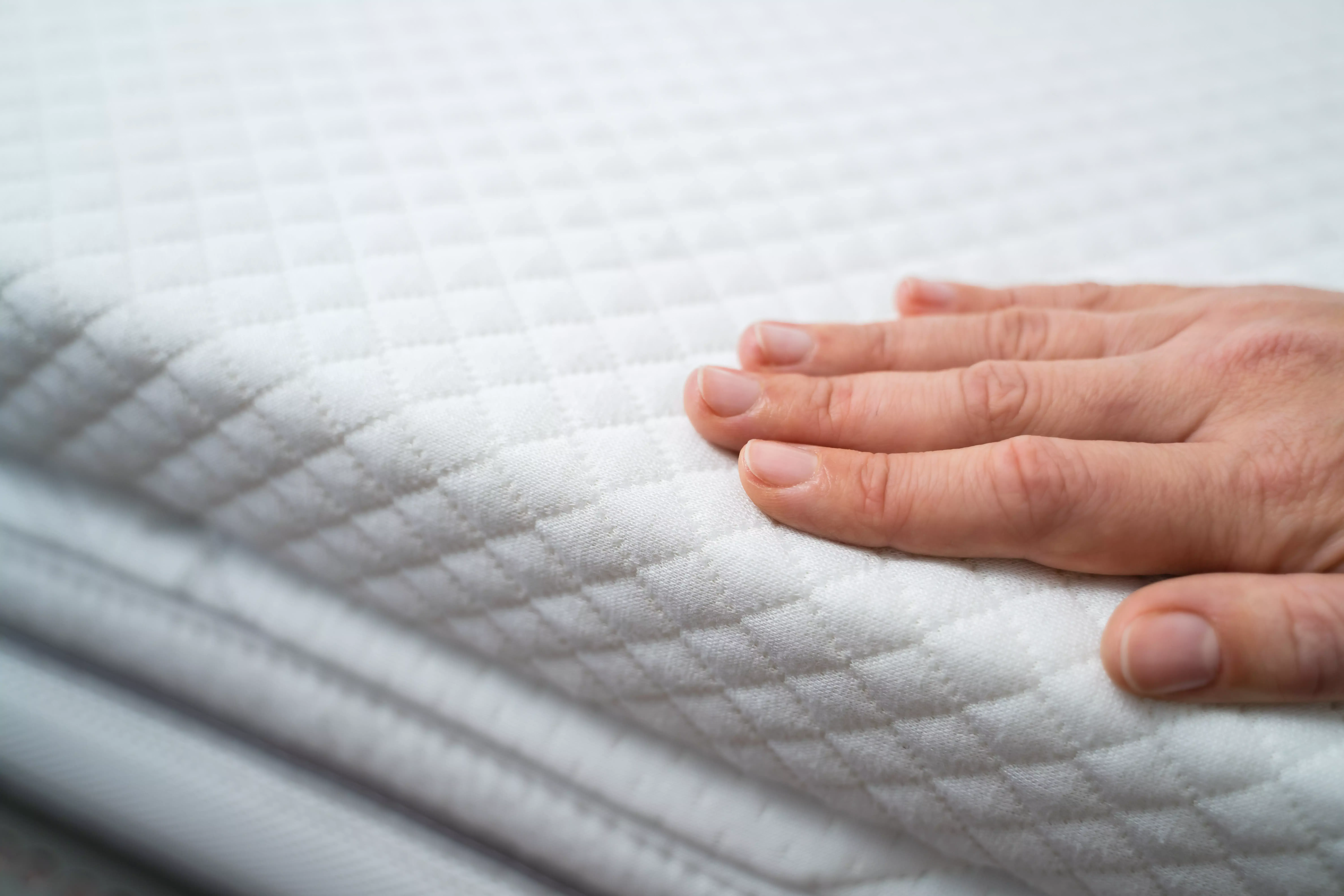 La main appuie doucement sur la surface d'un surmatelas matelassé - montre la surface douce et structurée pour un sommeil confortable.